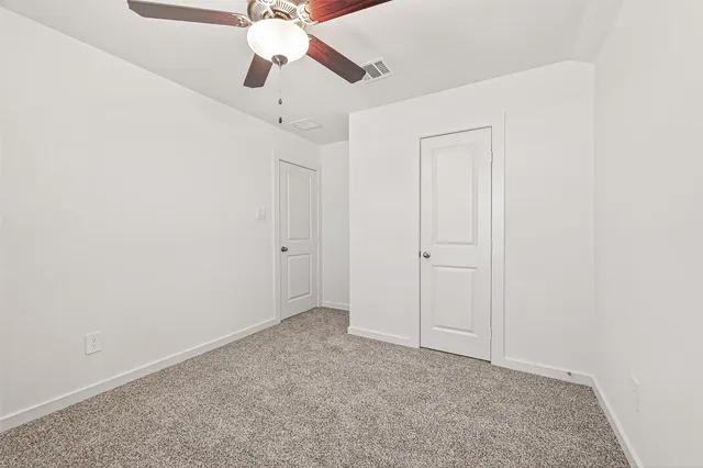 an empty room with a ceiling fan and carpet