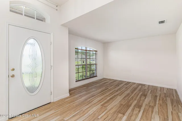 an empty room with wooden floor mirror and windows