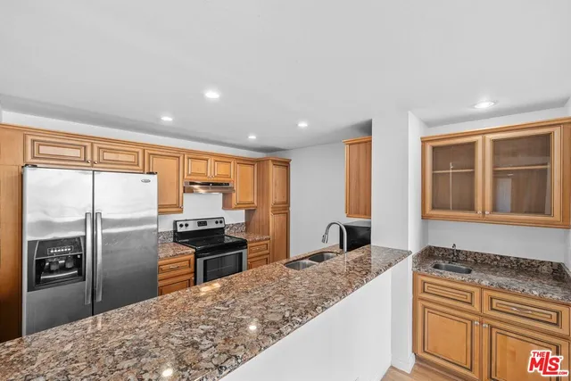a kitchen with stainless steel appliances granite countertop a refrigerator a stove and a sink with wooden floor
