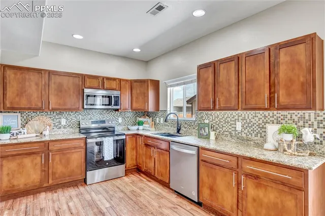 a kitchen with stainless steel appliances granite countertop wooden cabinets a sink dishwasher and a stove with wooden floor