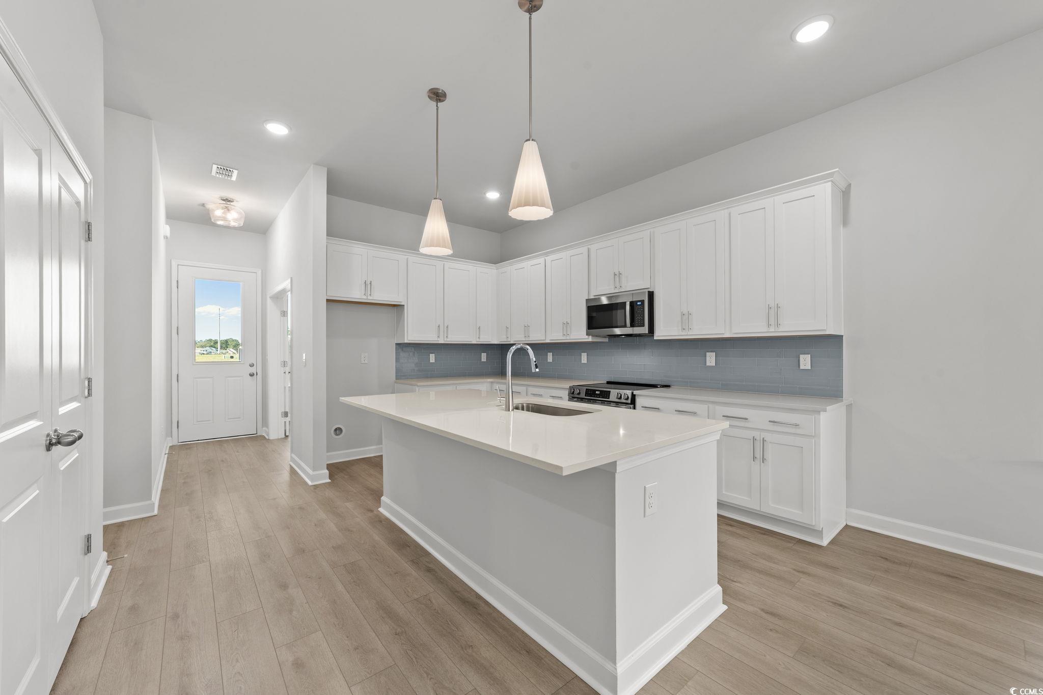 771 Ebb Tide Road Little River, SC 29566 - Photo 17 of 35 Kitchen featuring white cabinets, a center island with sink, pendant lighting, stainless steel appliances, and backsplash