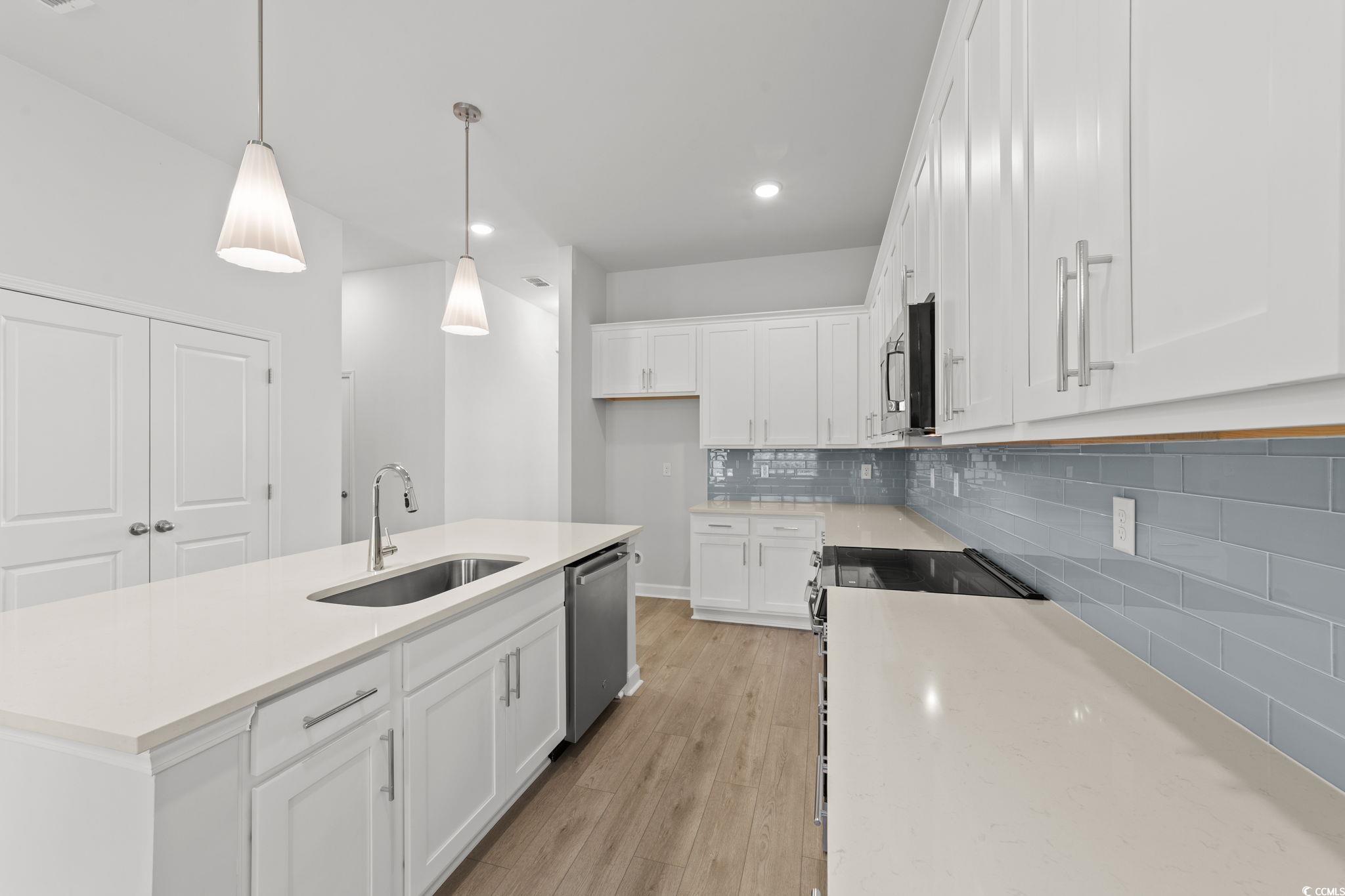 771 Ebb Tide Road Little River, SC 29566 - Photo 18 of 35 Kitchen with white cabinetry, decorative light fixtures, a center island with sink, decorative backsplash, and light stone counters