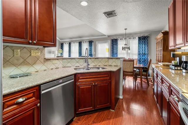 a kitchen with granite countertop wooden cabinets a sink dishwasher and a stove with wooden floor