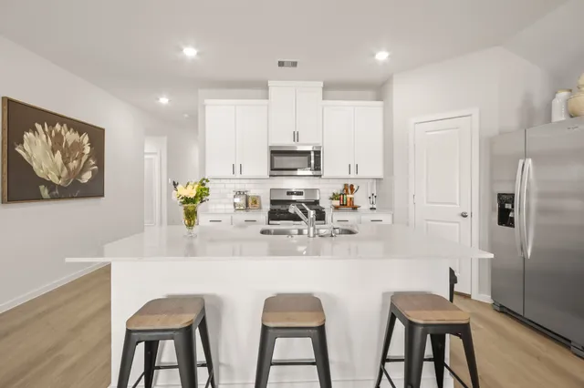 a kitchen with stainless steel appliances granite countertop a dining table chairs refrigerator and sink