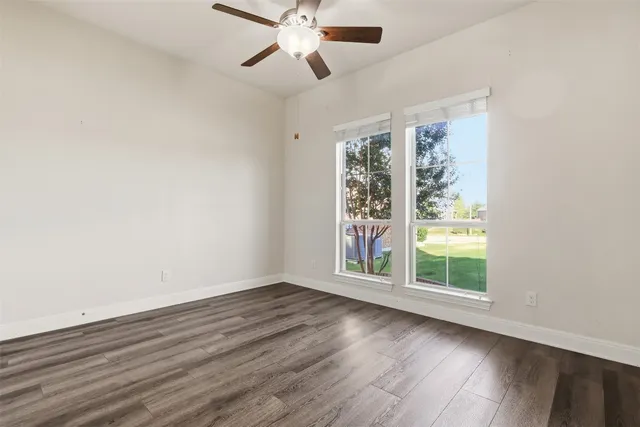 an empty room with wooden floor fan and windows