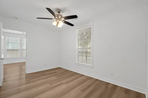 an empty room with wooden floor fan and windows
