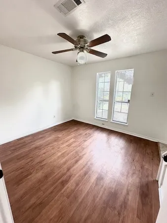 an empty room with wooden floor fan and windows