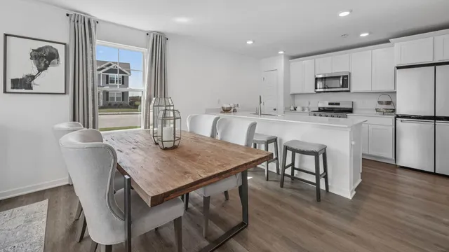 a kitchen with stainless steel appliances granite countertop a dining table chairs refrigerator and microwave