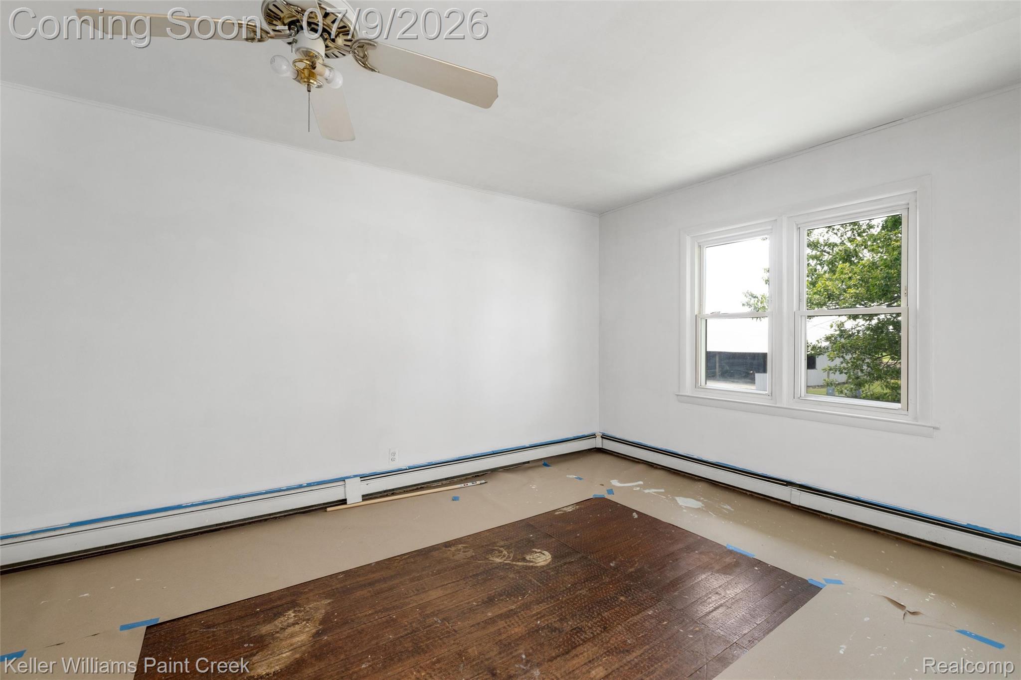 28780 School Section Road Richmond, MI 48062 - Photo 9 of 50 Bright interior space featuring a window with white trim, baseboard heating, a ceiling fan with light fixture, and a combination of exposed hardwood and subflooring