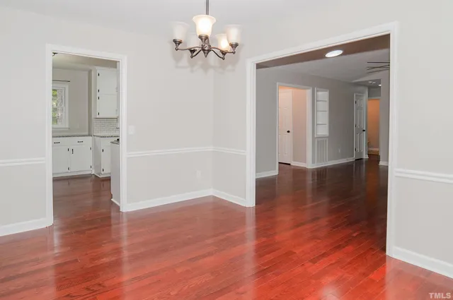 an empty room with wooden floor chandelier and windows