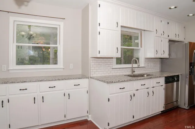 a kitchen with granite countertop a refrigerator a sink dishwasher a stove and white cabinets with wooden floor