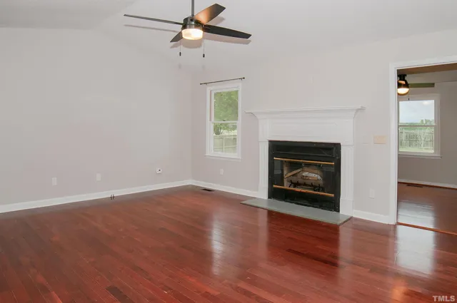 an empty room with wooden floor a fireplace and windows