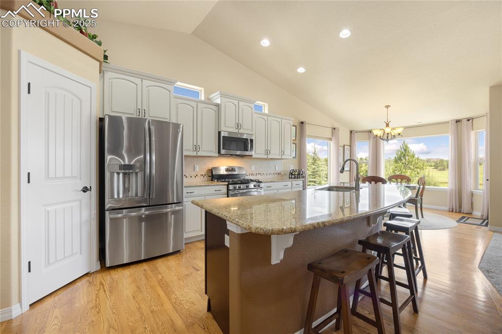 1131 Old North Gate Road Colorado Springs, CO 80921 - Photo 11 of 39 Kitchen with stainless steel appliances, a chandelier, vaulted ceiling, an island with sink, and light wood-type flooring