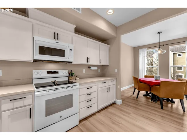 a kitchen with stainless steel appliances granite countertop a stove a sink dishwasher and white cabinets with wooden floor