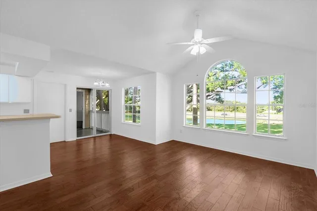 an empty room with wooden floor chandelier fan and windows