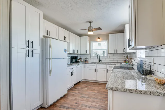 a kitchen with granite countertop a refrigerator a sink and white cabinets