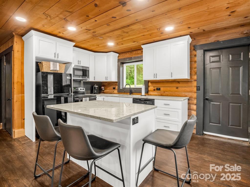 112 Bills Creek Road Lake Lure, NC 28746 - Photo 13 of 42 a kitchen with stainless steel appliances kitchen island granite countertop a stove a refrigerator a microwave oven with a dining table and chairs with wooden floor
