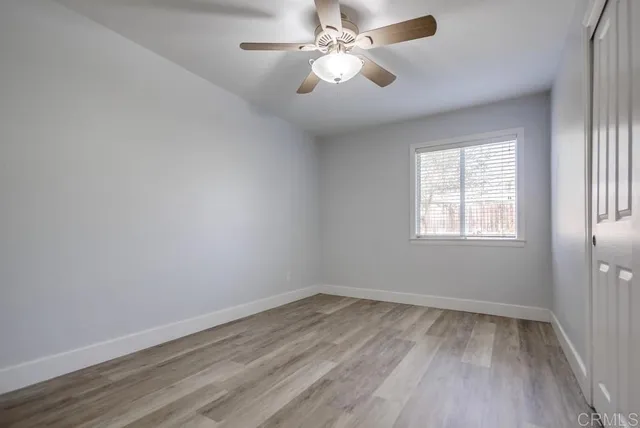 an empty room with wooden floor ceiling fan and windows