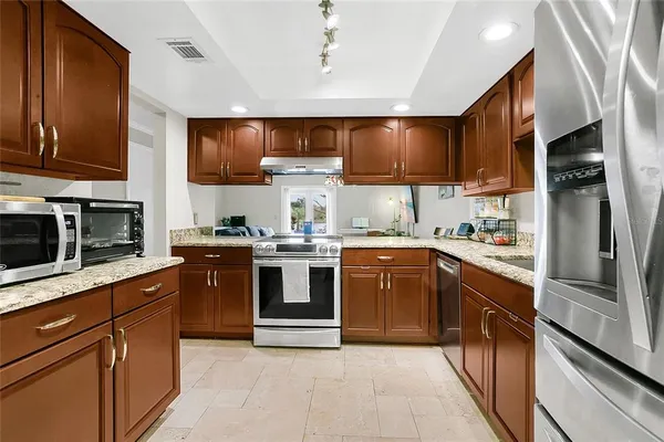 a kitchen with stainless steel appliances granite countertop a refrigerator a sink and wooden cabinets