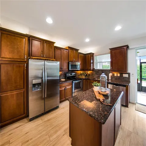 a kitchen with granite countertop stainless steel appliances a refrigerator a stove top oven and a refrigerator with wooden floor