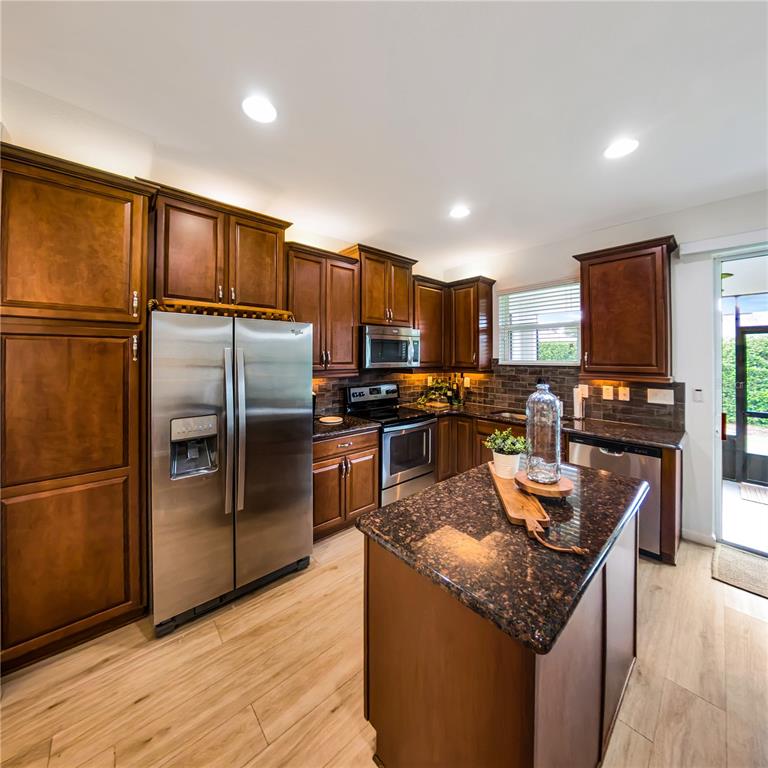 7235 Southwest 91st Court Ocala, FL 34481 - Photo 11 of 23 a kitchen with granite countertop stainless steel appliances a refrigerator a stove top oven and a refrigerator with wooden floor