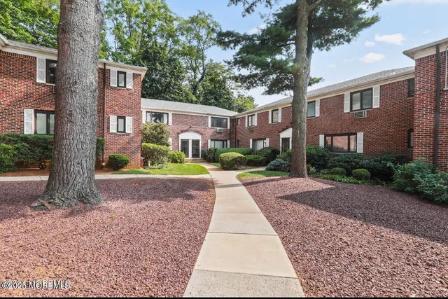 a view of a brick building next to a road with plants and trees