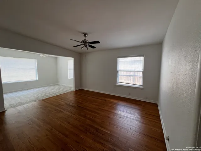 a view of empty room with wooden floor and fan