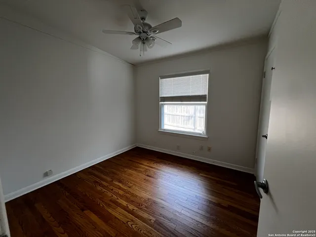 an empty room with wooden floor chandelier fan and windows