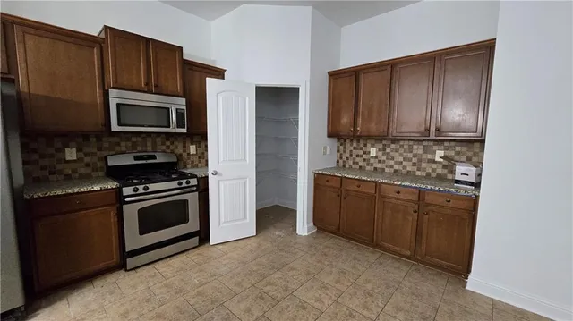 a kitchen with granite countertop wooden cabinets a stove a oven and a refrigerator with wooden floor