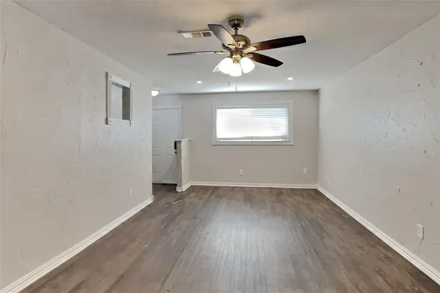 an empty room with wooden floor chandelier fan and windows