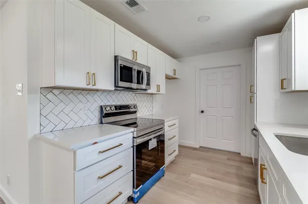 a kitchen with stainless steel appliances granite countertop grey cabinets a stove top oven a sink and dishwasher