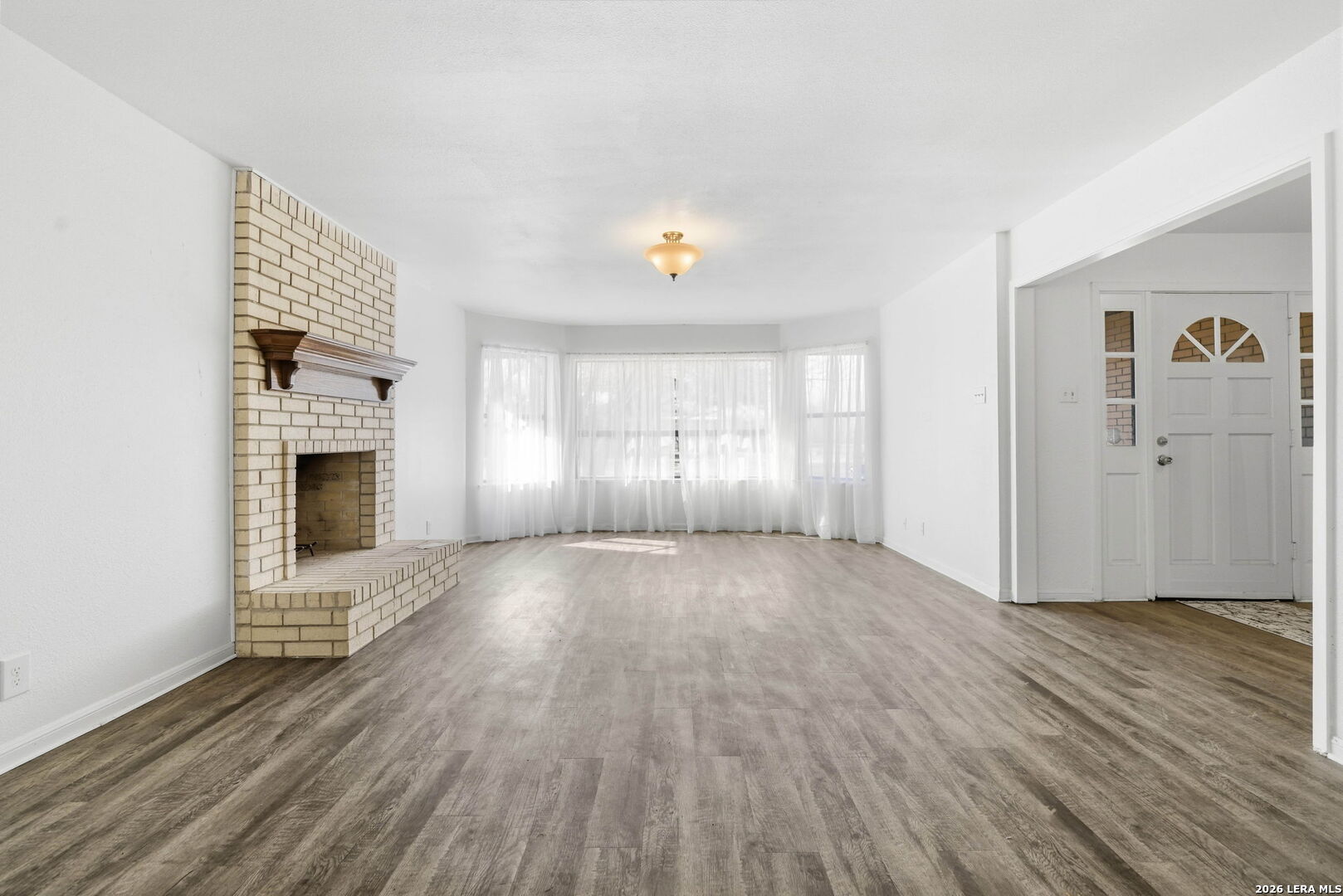 508 Crouch Avenue Devine, TX 78016 - Photo 4 of 26 an empty room with wooden floor fireplace and windows