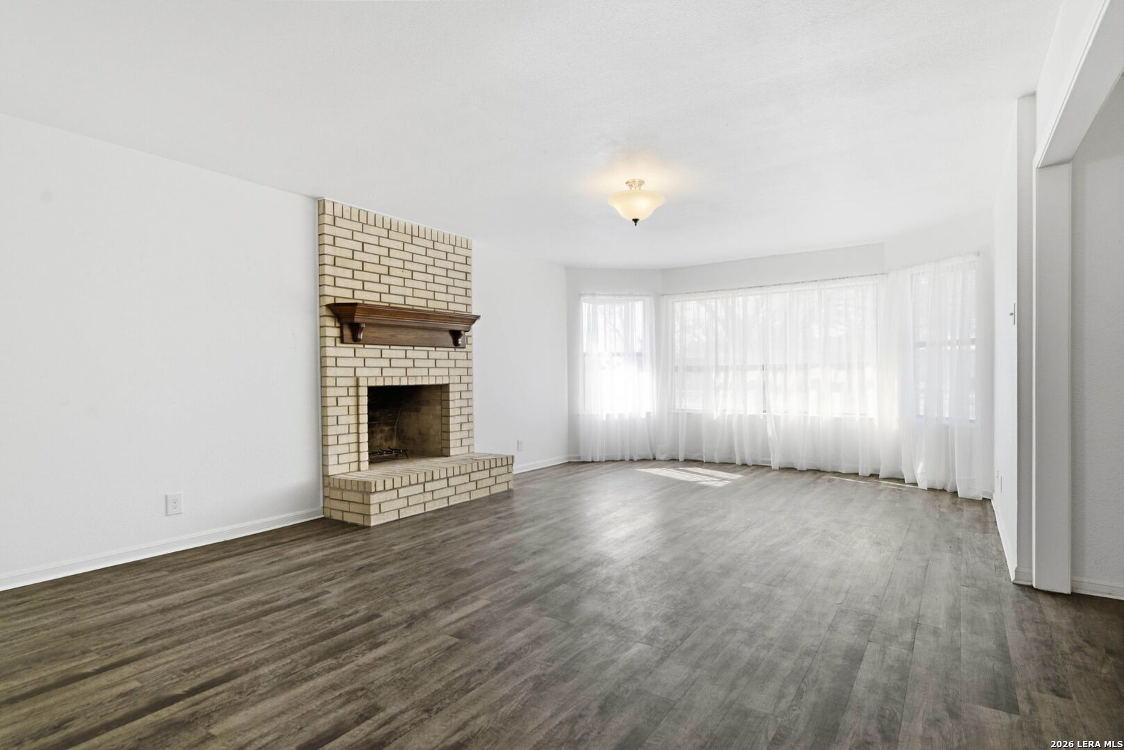 508 Crouch Avenue Devine, TX 78016 - Photo 5 of 26 an empty room with wooden floor fireplace and windows