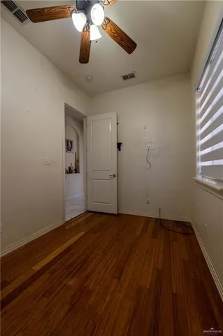 an empty room with wooden floor chandelier fan and windows