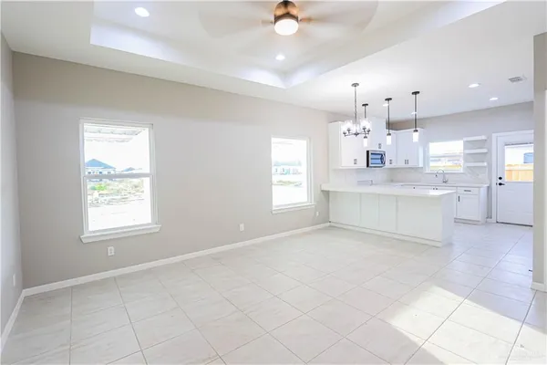 an empty room with kitchen view and a chandelier fan