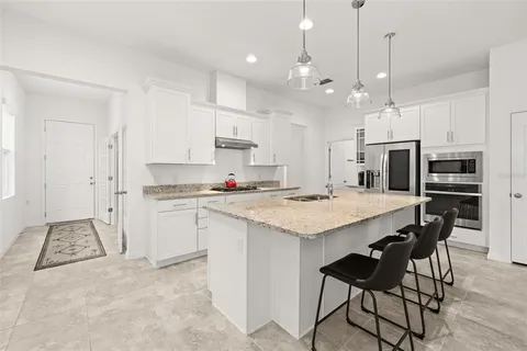 a kitchen with stainless steel appliances granite countertop a sink a stove a refrigerator and white cabinets with wooden floor