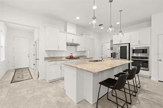 a kitchen with stainless steel appliances granite countertop a sink a stove a refrigerator and white cabinets with wooden floor