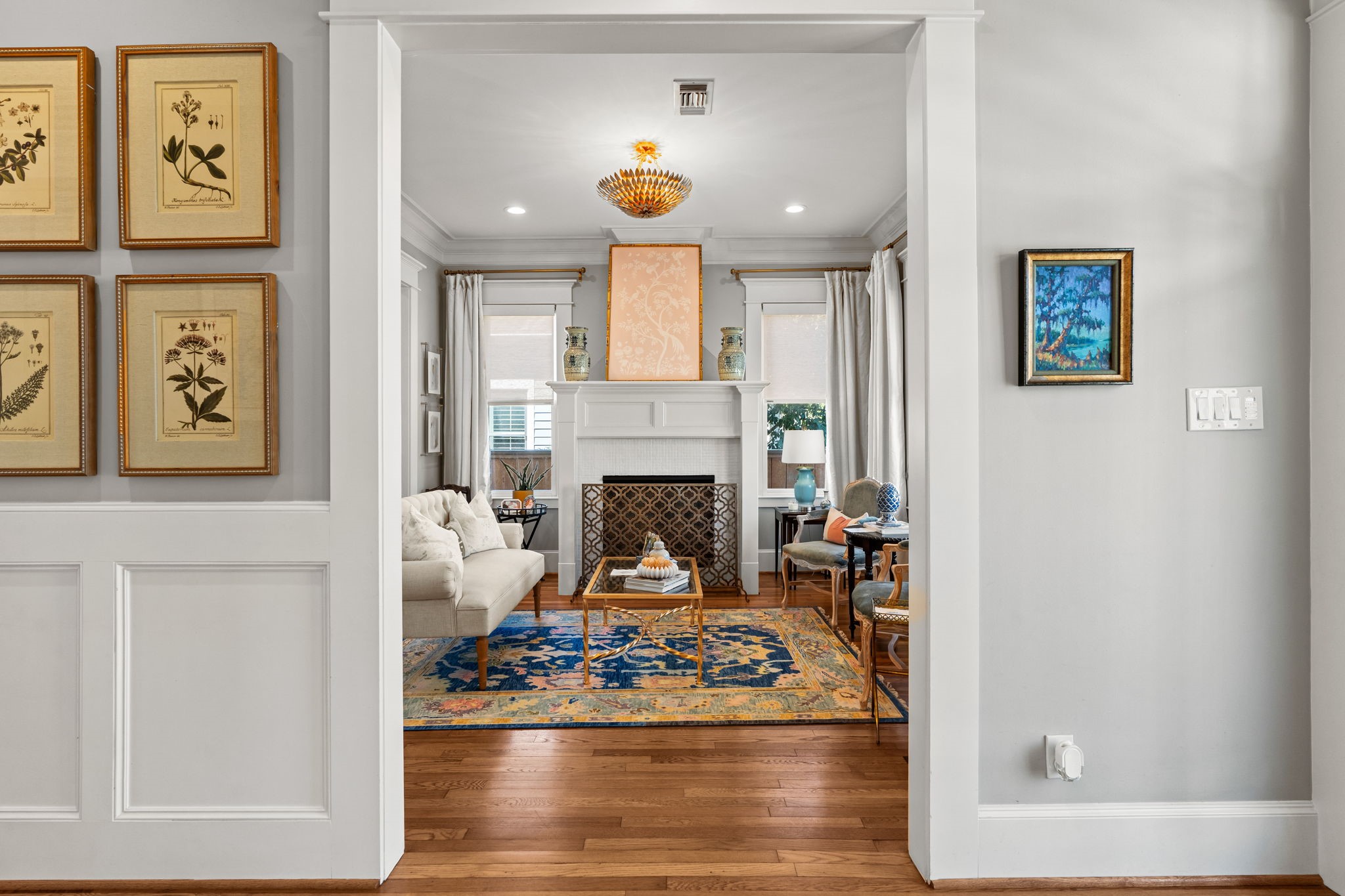 1236 Omar Street Houston, TX 77008 - Photo 2 of 50 Just off the entry, formal living room showcases rich hardwood flooring, wainscoting, detailed crown molding, and abundant natural light. The fireplace serves as a focal point, framed by classic millwork and symmetrical windows.