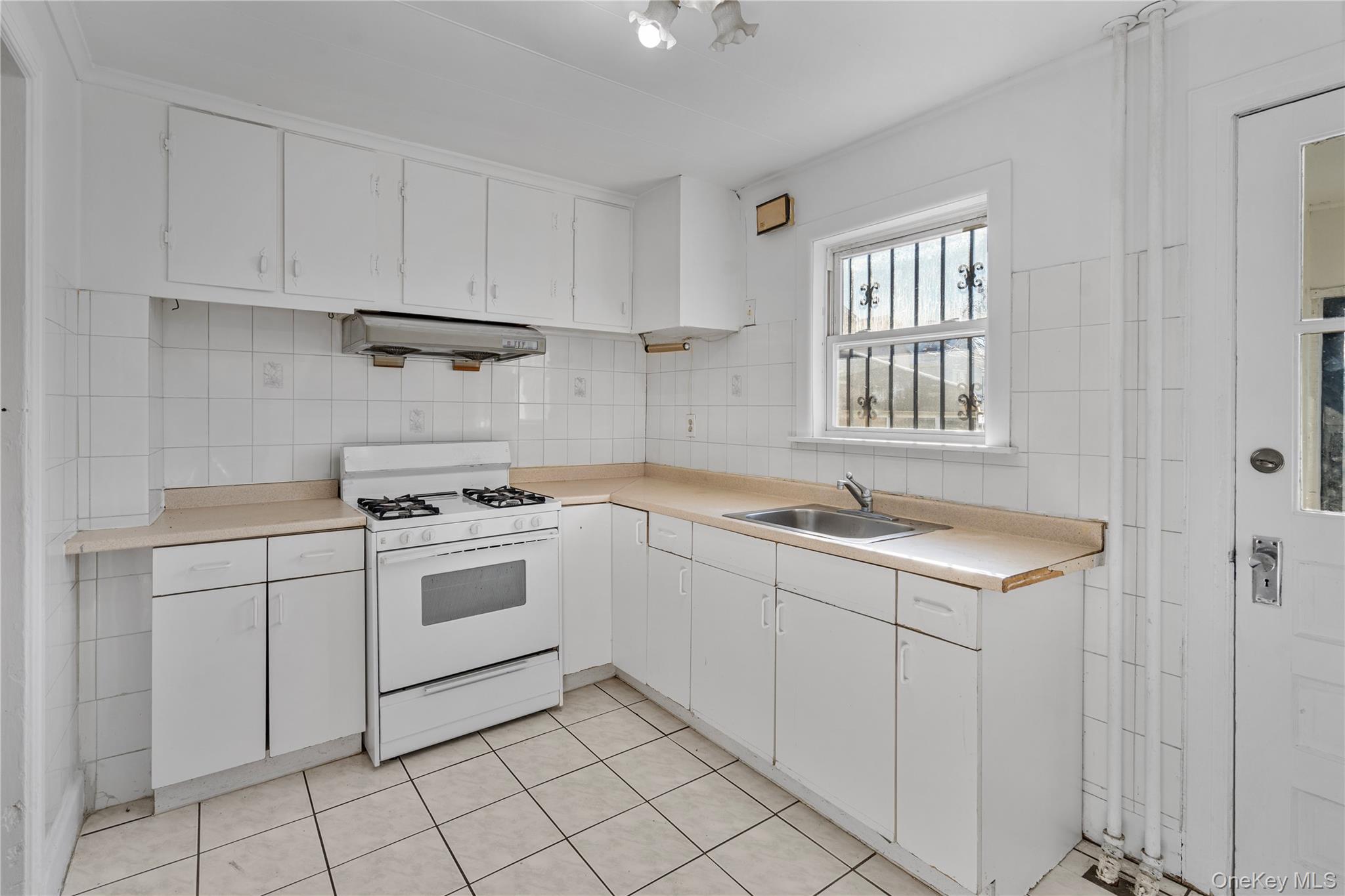 123-10 25th Road Queens, NY 11354 - Photo 5 of 27 Kitchen with white range with gas stovetop, light countertops, white cabinetry, light tile patterned floors, and tile walls