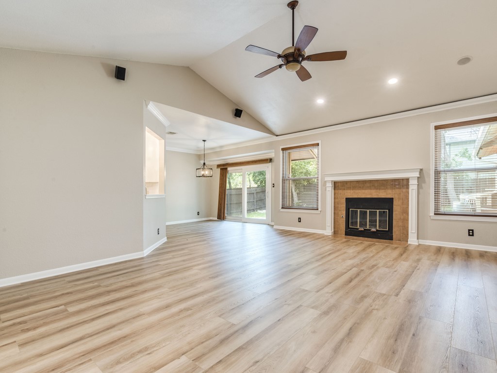 Unfurnished living room with a ceiling fan, a tiled fireplace, light wood-type flooring, and ornamental molding