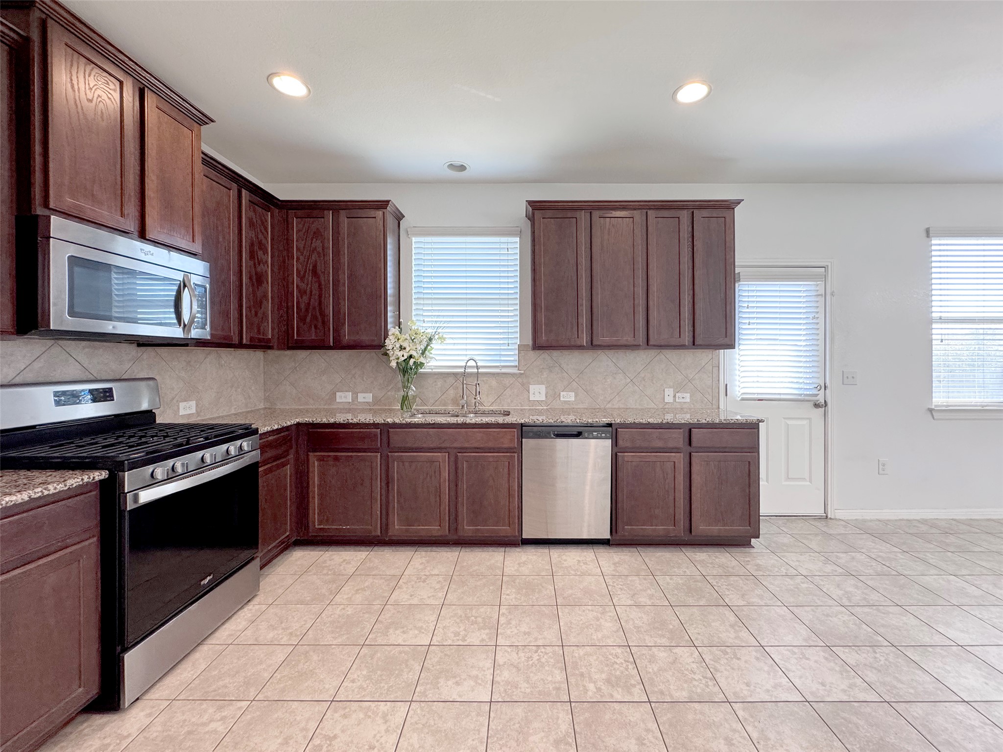 251 Triumph Road Buda, TX 78610 - Photo 9 of 24 Kitchen with stainless steel appliances, dark wood finish cabinetry, light stone counters, light tile patterned flooring, and tasteful backsplash