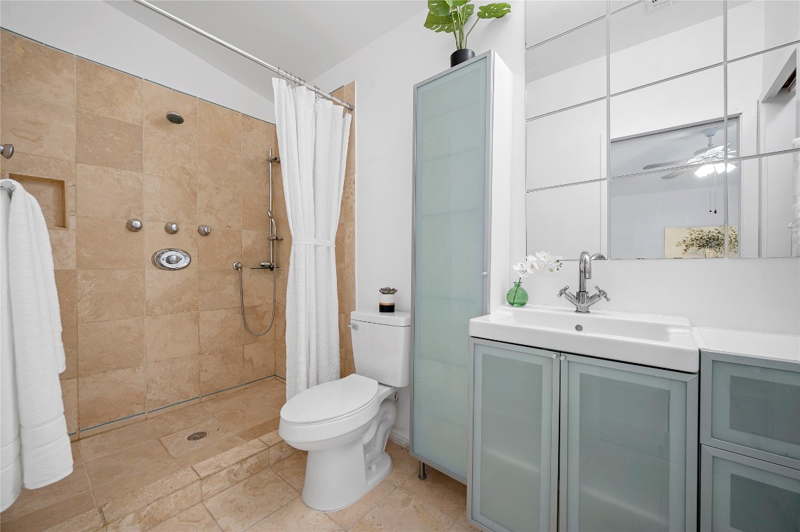 primary bathroom with large walk in shower with multiple shower heads, sleek cabinets with glass fronts