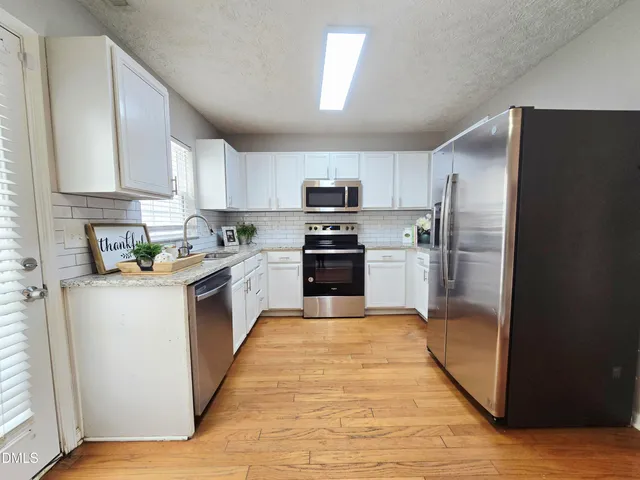 a large kitchen with stainless steel appliances granite countertop a refrigerator a sink dishwasher a stove top oven a kitchen island and cabinets with wooden floor