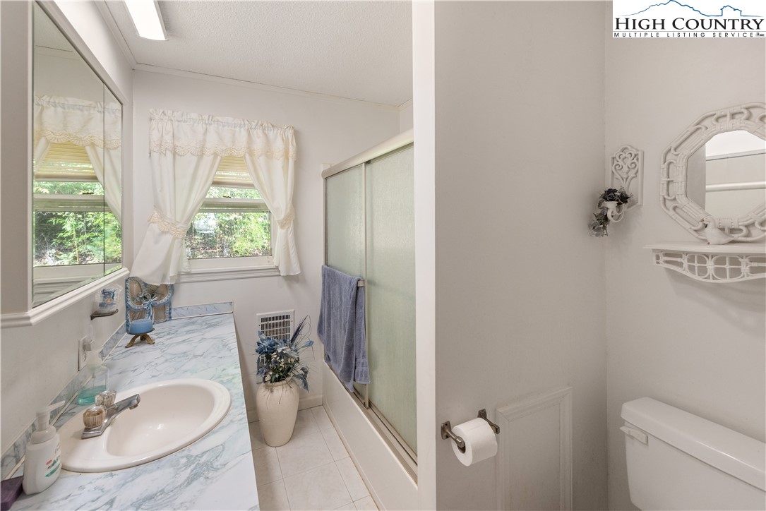 4934 Silas Creek Road Lansing, NC 28643 - Photo 28 of 32 a bathroom with a granite countertop sink a toilet and a window