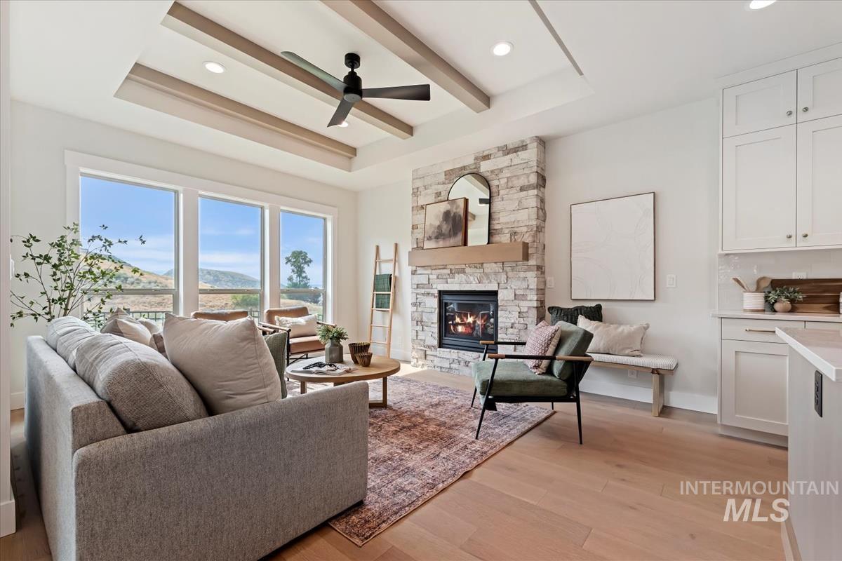 2166 East Rodeo Street Kuna, ID 83634 - Photo 6 of 43 Great room featuring a stone-clad fireplace with wood mantel, a recessed ceiling with exposed beams and a ceiling fan, and light wood-finish flooring