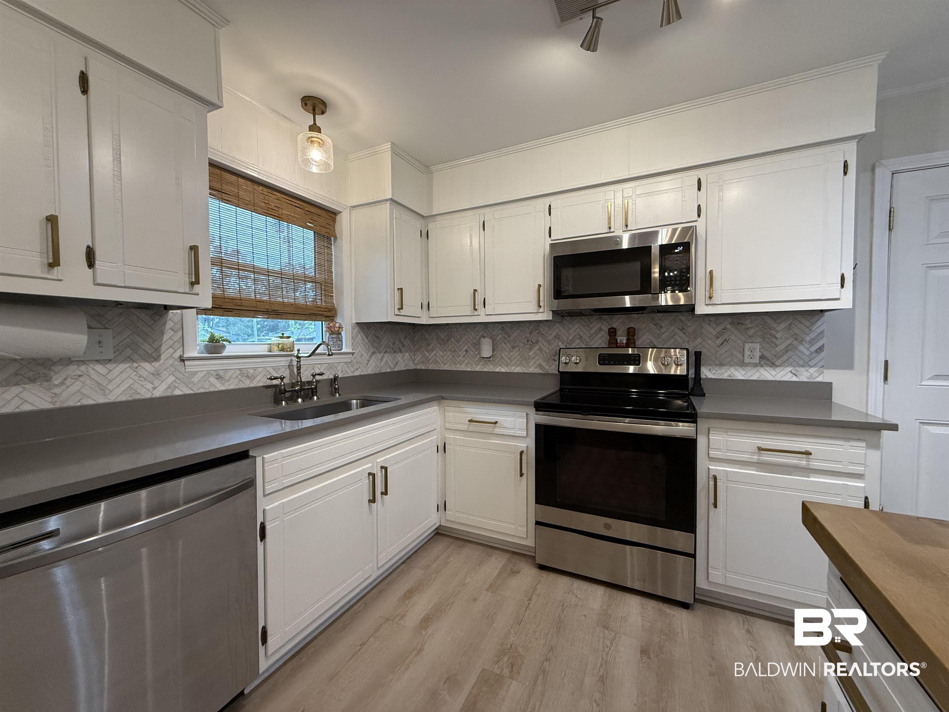 90 Florida Street Monroeville, AL 36460 - Photo 18 of 31 Kitchen featuring appliances with stainless steel finishes, sink, white cabinets, decorative backsplash, and light hardwood / wood-style flooring