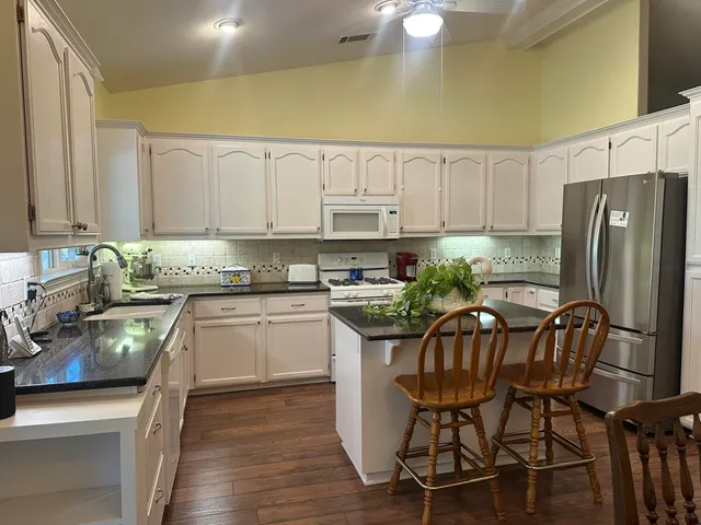 a kitchen with stainless steel appliances granite countertop a stove a refrigerator a sink a stove and white cabinets with wooden floor