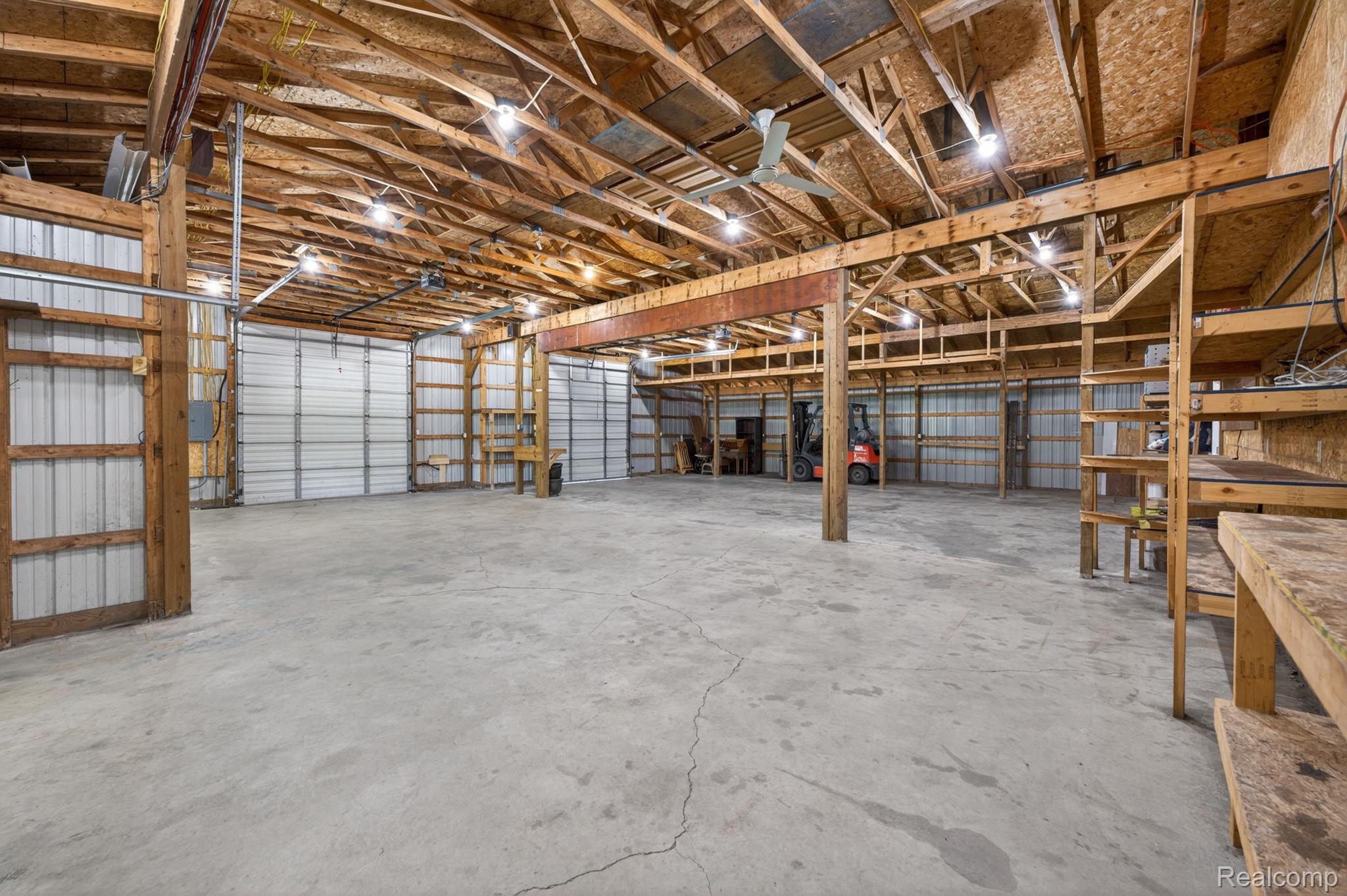 9353 Hill Road Swartz Creek, MI 48473 - Photo 75 of 98 Large open-concept interior featuring concrete flooring, exposed wood beam ceiling, multiple overhead lighting fixtures, ceiling fans, and several garage doors