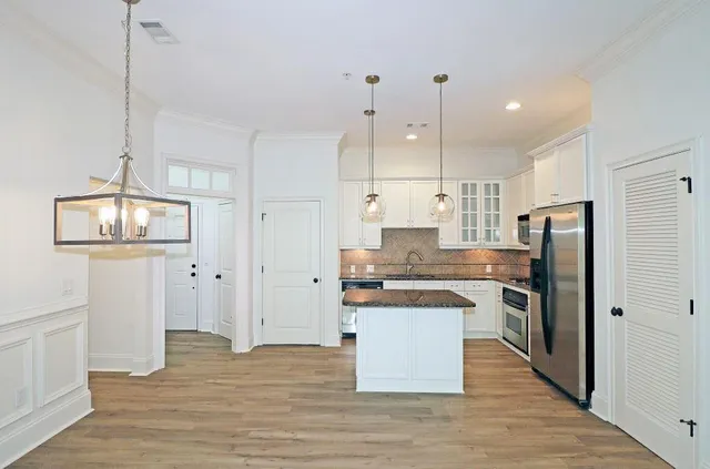 a kitchen with stainless steel appliances granite countertop a refrigerator a sink dishwasher a stove and white cabinets with wooden floor