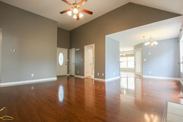 a view of an empty room with wooden floor and a fan